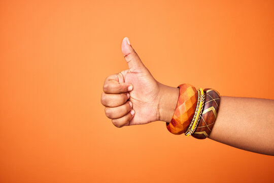 Hand, thumbs up and person with arm on orange background for thank you or confirm with gesture or sign. Good news, expression and positive with yes or thanks with win in studio for agreement.