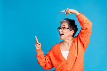 Wall Mural - Portrait of aged lady direct fingers empty space wear orange cardigan isolated on blue color background