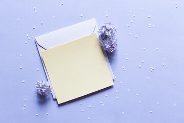 Wall Mural - Mother's day banner with blank white card, envelope and bouquet of lilac flowers and petals on blue background