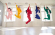 Full length portrait of happy smiling young people in bright colorful suits jumping with hands up together in a row indoors. Cheerful guys and girls in fashionable stylish party outfit.