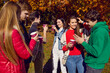 Happy friends having fun standing together with drinks in park. Group of joyful friends celebrating outdoors and toasting with paper cups. Cheerful friends having good time together in autumn park