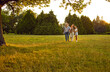 Happy family spending time outdoors. Parents and kids strolling in nature. Mother, father and children enjoying quiet summer evening and walking together on green lawn in beautiful city park or garden