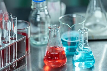 image shows two graduated conical flasks containing red and blue liquids on a lab table.