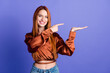 Photo of pretty young woman point finger arm hold empty space wear brown shirt isolated on violet color background