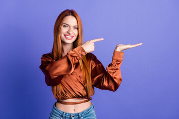 Wall Mural - Photo of pretty young woman point finger arm hold empty space wear brown shirt isolated on violet color background