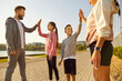 Happy smiling sporty family with children giving high five each other rejoicing the success in sport training or exercise achievement standing outdoors in park after workout in nature.