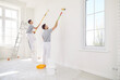 Male painters or construction workers painting walls in white color with paint roller brush, professional service team on stepladder wearing protective uniform finishing task for room, building repair