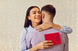 Happy loving couple, woman hugging man holding red gift box, getting romantic present. Sharing love moment feelings, Valentine day emotion, loving male, female pair, young people celebrate holiday 