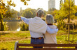 Old love is truest love. Romantic senior couple in love on date talking while sitting on park bench. Back view of mature man hugging his wife and showing her something from distance on warm evening.