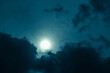 Cloudy night sky with shining full moon through the dark clouds.