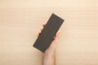 Young adult man hand holding and showing new dark black sandpaper sponge on light ash veneer wooden surface background. Closeup. Preparing material for repair work of home. Top down view.