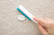 Young adult woman hand holding brush and removing chewing gum from light beige home carpet. Closeup. Top down view.