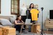 © itchaznong - Asian woman friends couple talk to camera to sell the clothes at home. Young attractive business people female live streaming and showing clothing to customer in online