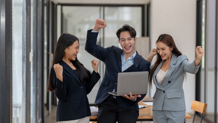 Wall Mural - Group young Asian business people raising his hand to congratulate excited and happy at a successful work with laptop computer at office Asian business people raising his hand to congratulate excited