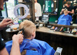 Hairdresser using electric shaver to cut boy's hair. Little kid getting first haircut in barbershop. Close up