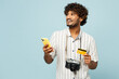 © ViDi Studio - Traveler Indian man wear white casual clothes hold credit bank card mobile cell phone isolated on plain blue background. Tourist travel abroad in free spare time rest getaway. Air flight trip concept.