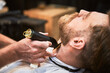 Close-up of professional barber trimming client's beard. Male hairdresser serving client with thin beard by clipper. Isolated photo of man getting his haircut done.