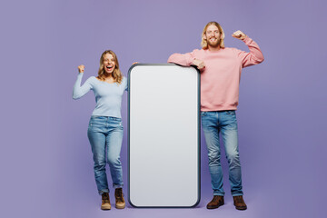Wall Mural - Full body young couple two friend family man woman wear pink blue casual clothes together big huge blank screen area mobile cell phone smartphone do winner gesture isolated on plain purple background