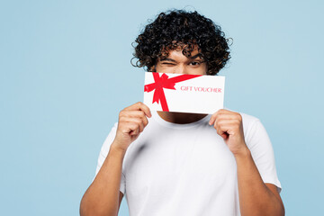 Wall Mural - Young happy Indian man he wear white t-shirt casual clothes hold gift certificate coupon voucher card for store isolated on plain pastel light blue cyan background studio portrait. Lifestyle concept.