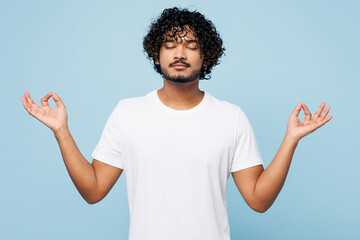 Wall Mural - Young Indian man wear white t-shirt casual clothes hold spreading hands in yoga om aum gesture relax meditate try to calm down isolated on plain pastel light blue cyan background. Lifestyle concept.