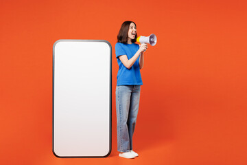 Wall Mural - Full body young woman wear blue t-shirt casual clothes big huge blank screen mobile cell phone smartphone with workspace copy space mockup scream in megaphone isolated on plain red orange background.