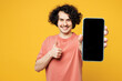 Young smiling man he wears pink t-shirt casual clothes hold in hand use mobile cell phone with blank screen workspace area show thumb up isolated on plain yellow orange background. Lifestyle concept.