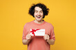 Young surprised shocked happy man he wear pink t-shirt casual clothes hold gift certificate coupon voucher card for store isolated on plain yellow orange background studio portrait. Lifestyle concept.