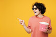 Young smiling amazed happy man he wear pink t-shirt casual clothes 3d glasses watch movie film hold bucket of popcorn in cinema point finger aside isolated on plain yellow background studio portrait.