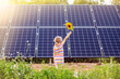 Young 6 year old blonde girl child standing in front of small solar panel farm in countryside. Renewable energy concept. Sun lens flare.