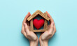saving hands holding a wooden house with red heart inside