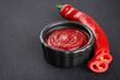 Gochujang Korean traditional spicy fermented sauce in a bowl and chili pepper on a dark background.