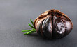 Bulb of black garlic and rosemary on  gray background.