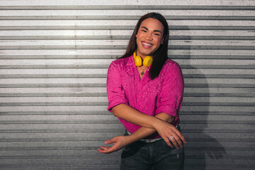 Portrait of trans woman with pink shirt and yellow headphones over gray background.. LGBT people.