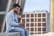 © Paula - Man on vacation in the city typing on his mobile phone. Happy and smiling man sending messages with his phone. Boy sitting looking at his social media and using apps on his phone.