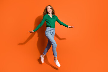 Wall Mural - Full length photo of dreamy excited lady dressed green shirt jumping walking emtpy space isolated orange color background