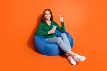 Sticker - Full length photo of friendly cute lady dressed green shirt waving arm hi texting modern device isolated orange color background