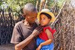 African village, father with a loving face and gesture holding a cute little girl with a straw hat, in front of the outdoors kitchen,