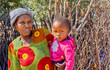 African village, happy granny woman with a big smile wrinkles holding her grandchild in front of the outdoors kitchen, in the yard
