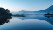 Calm lake at dawn reflecting a mist-covered mountain range, creating a tranquil and serene atmosphere.

