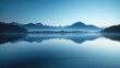 Calm lake at dawn reflecting a mist-covered mountain range, creating a tranquil and serene atmosphere.
