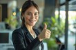 © Maelgoa - A confident businesswoman giving a thumbs up in the office