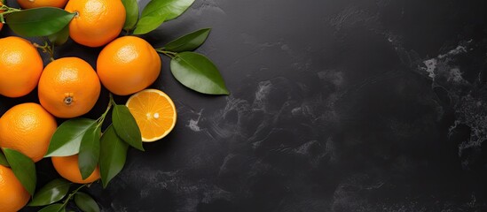 Poster - Top view of a flat lay fruit composition featuring an orange or tangerine with leaves placed on a black stone background The image provides copy space for text or other elements