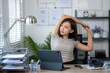 © Wasana - A woman is stretching her arms in front of a computer. She is wearing a grey shirt and is sitting in front of a desk with a laptop and a keyboard