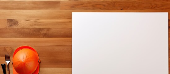 Wall Mural - A top down view of a brown wooden table displaying a white sheet of paper alongside an orange safety helmet a notepad or notebook and a cup of coffee The image offers ample space for text or any desi