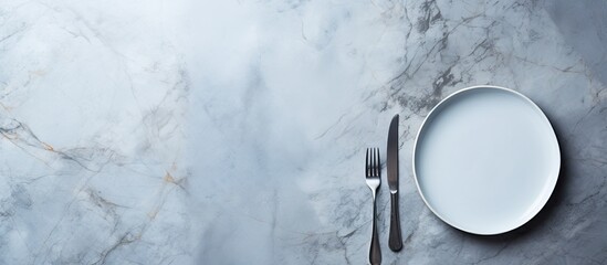 Poster - A light grey marble table is shown in a flat lay style featuring an empty blue plate accompanied by cutlery and a napkin Copy space image available
