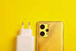 Smartphone with charging adapter on yellow background. Top view