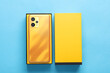 Modern yellow new smartphone with box on blue background. Top view