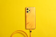 Yellow smartphone with a connected cable on a yellow background. Top view