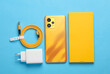 New yellow smartphone with box and accessories on blue background. Modern gadgets, unboxing. Flat lay. Top view