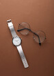 Stylish wristwatch with eyeglasses on a brown background. Women's accessories. Top view